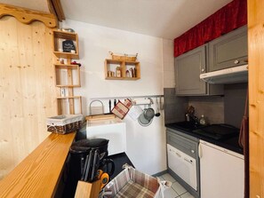 A compact kitchen with wooden cabinets, a coffee maker, and a hanging pot rack. - Cozy chalet-style studio near slopes with balcony (Les Belleville)
