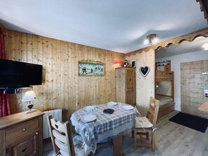 A cozy room with wooden walls, a dining table set for two, a television, and a bunk bed. - Cozy chalet-style studio near slopes with balcony (Les Belleville)