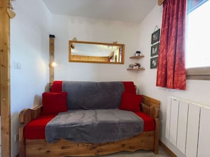 A wooden sofa with red and grey cushions, a wooden-framed mirror, and a radiator on the wall. - Cozy chalet-style studio near slopes with balcony (Les Belleville)