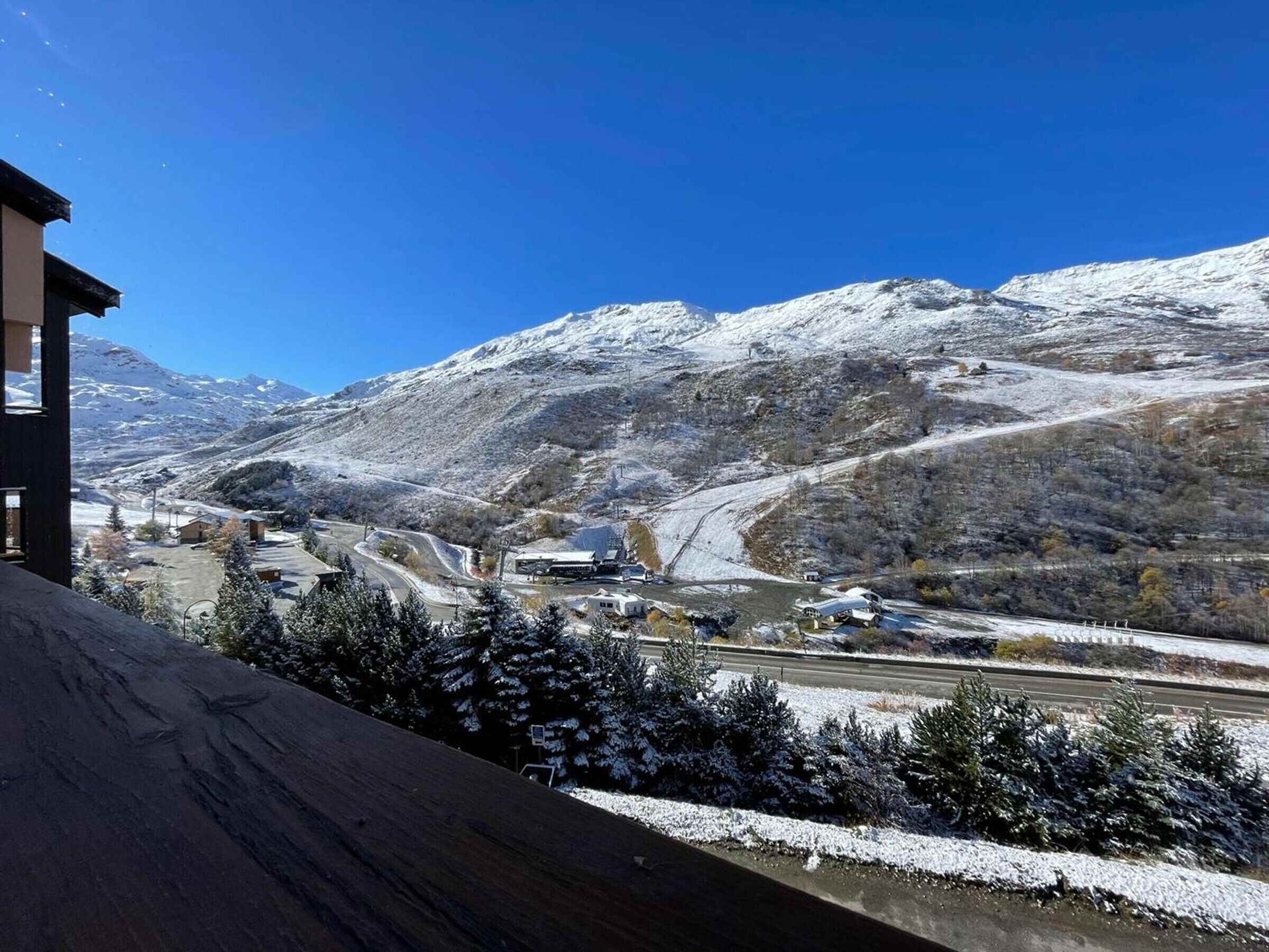 Paisagem montanhosa com picos cobertos de neve e uma estrada serpenteando por um vale.