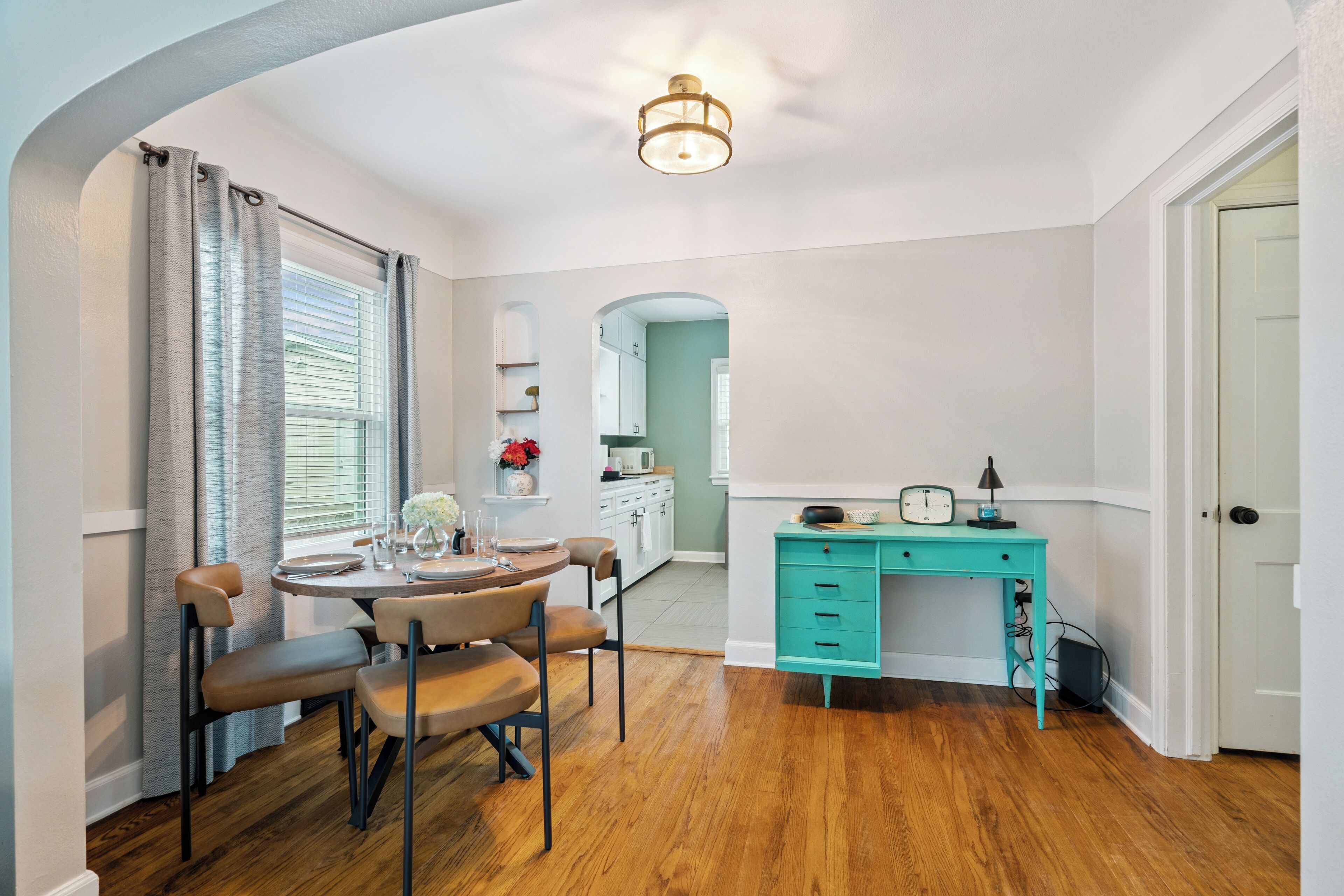 Un coin repas avec une table ronde et des chaises, une cuisine en arrière-plan et un bureau turquoise avec des tiroirs.