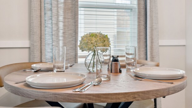 Een eettafel gedekt met borden, bestek, glazen en een vaas met bloemen.