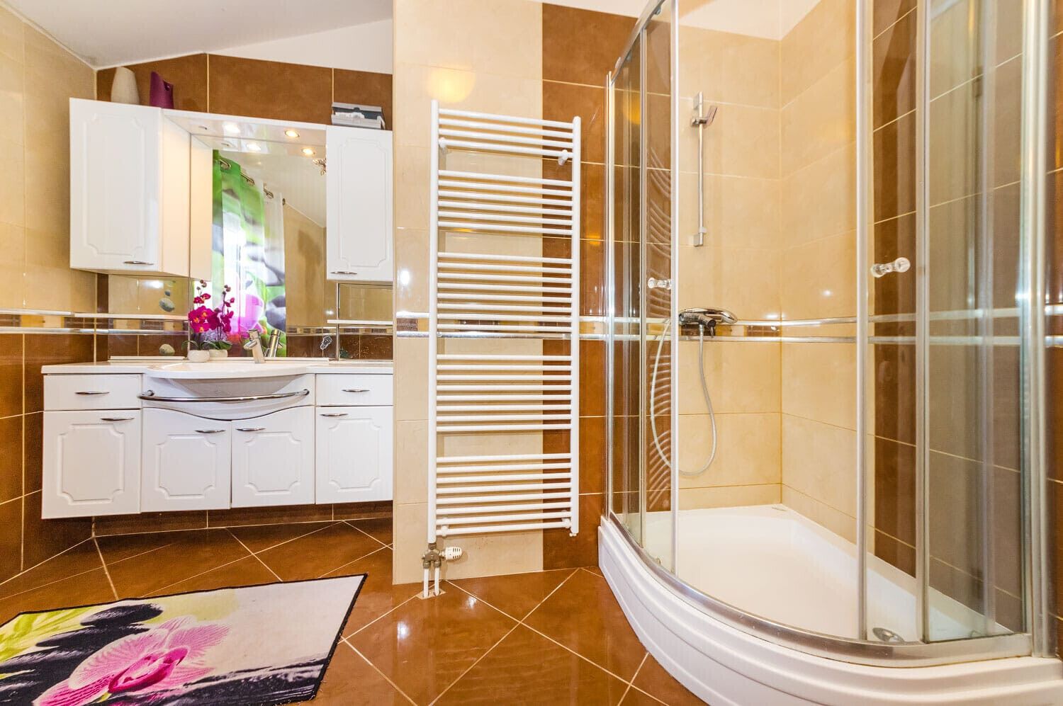 Une salle de bain moderne avec une douche à l’italienne en verre, un meuble-lavabo blanc avec un miroir et un tapis décoratif.