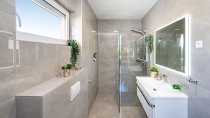 A modern bathroom with a glass shower enclosure, a vanity with a mirror, and potted plants. - Villa Renata ZadarVillas (Zaton)