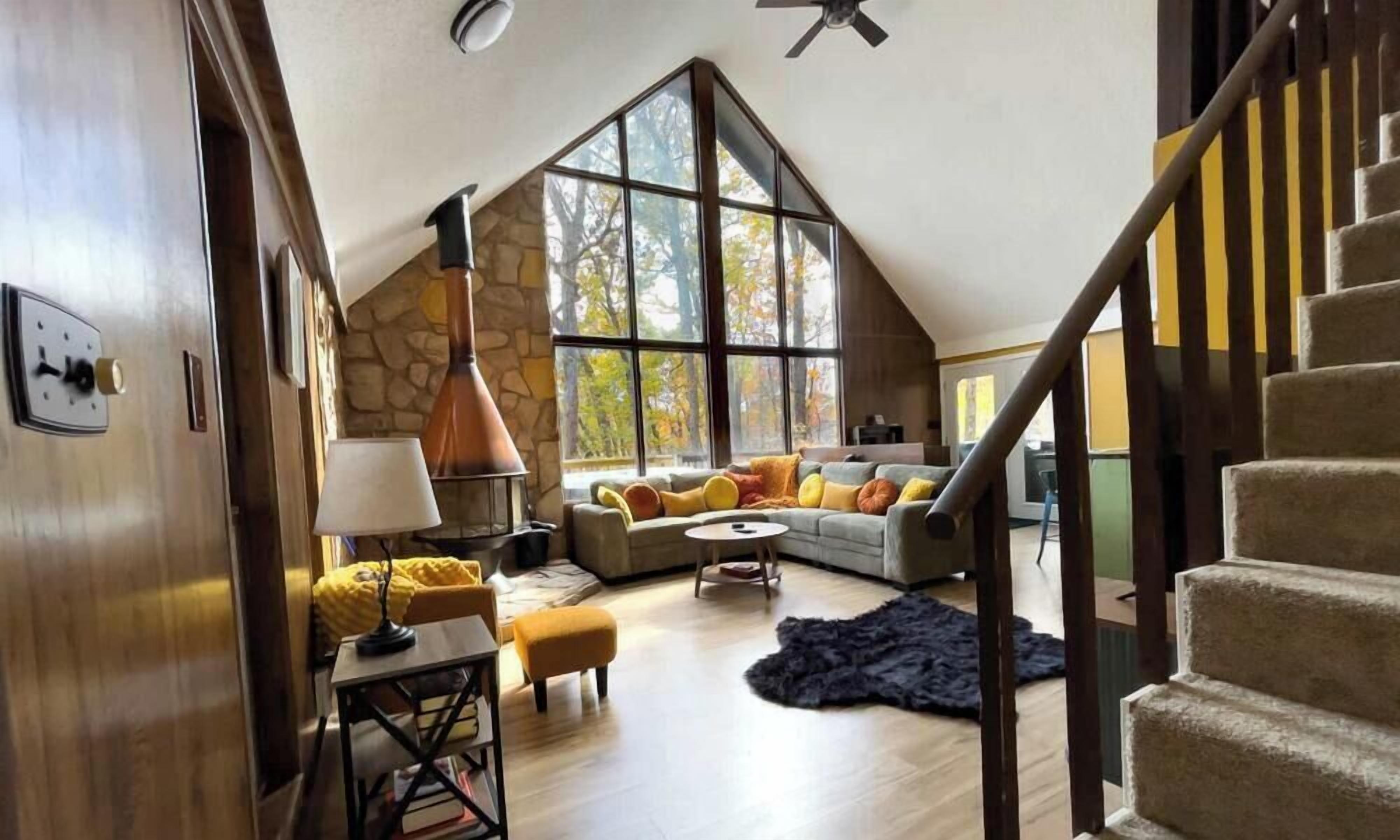 A loft-style living room with a stone wall, a large window, a staircase, and a cozy seating area.