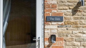 Un muro de piedra con un letrero que dice "The Den" y una puerta que da al interior.