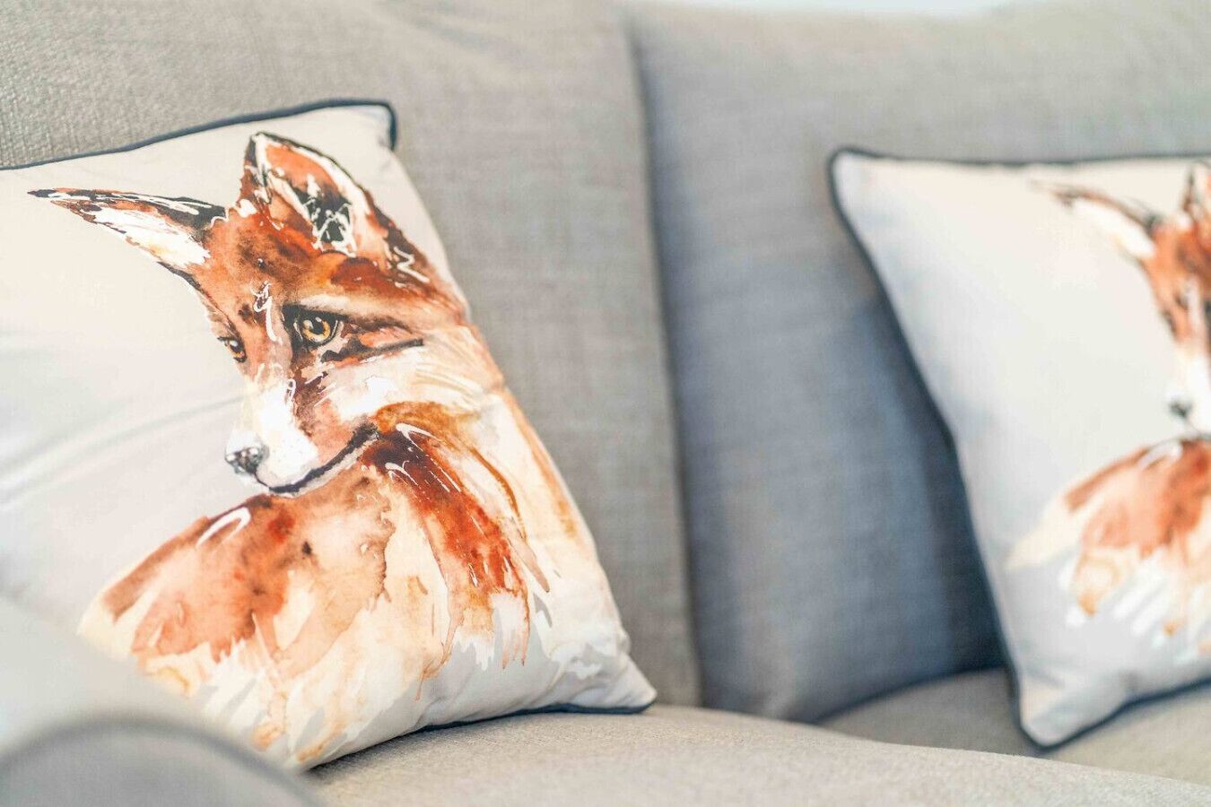 Two pillows with a fox design on a grey sofa.