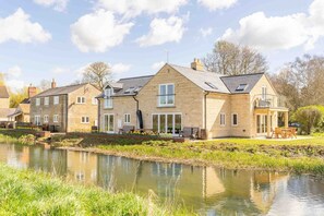 A stone house with a pond in front, large windows, and a patio with outdoor furniture. - The Holt: beauty by the river (Stamford)