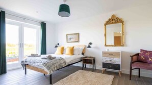 Une chambre à coucher comprenant un lit, des tables de chevet, une commode, un miroir et une vue sur l’extérieur.