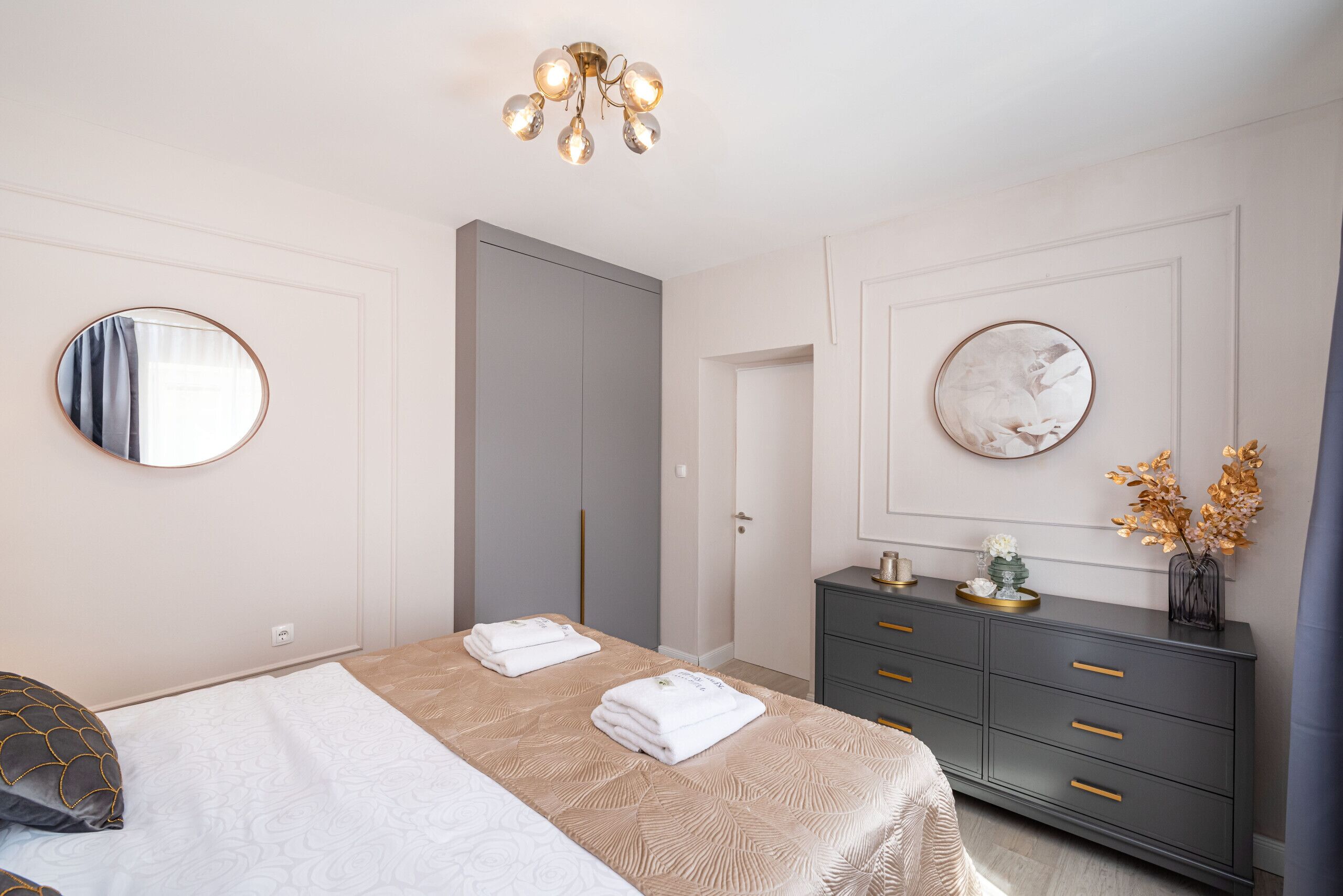 Une chambre à coucher avec un lit, deux tables de chevet, une commode, un miroir et une porte.
