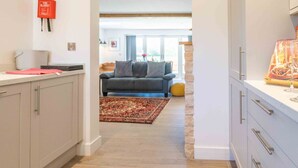 A modern kitchen with light-colored cabinets, a red fire blanket on the wall, and a dining area with a sofa and rug. - The Roost: a riverside retreat (Stamford)