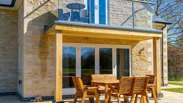 A wooden deck with a glass door entrance, stone walls, and outdoor furniture. - The Roost: a riverside retreat (Stamford)