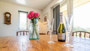 A wooden dining table with a bottle of Prosecco wine, two wine glasses, and a vase with pink roses. - The Roost: a riverside retreat (Stamford)