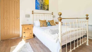 A bedroom with a bed, wooden nightstand, and a painting on the wall. - The Sett: cosy riverside home (Stamford)