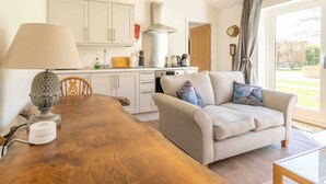 A modern kitchen with white cabinets, a wooden dining table, and a beige sofa with colorful cushions. - The Sett: cosy riverside home (Stamford)