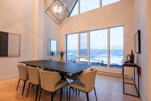 Ein Essbereich mit großem Tisch, Stühlen und Blick durch große Fenster.