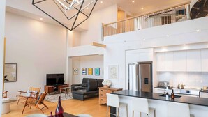 Un amplio salón con un gran comedor de mármol, una lámpara de araña moderna y una cocina con armarios blancos y electrodomésticos de acero inoxidable.