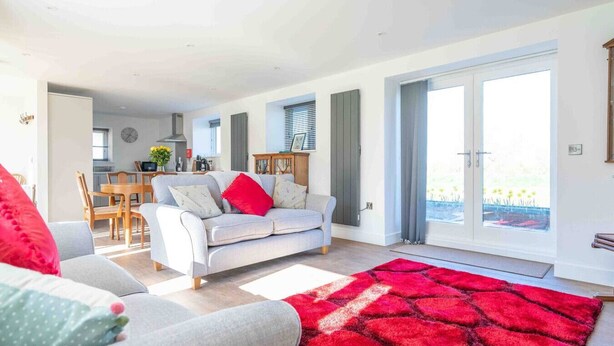 Un salon moderne avec un canapé, des fauteuils et un tapis rouge. On y trouve également un coin repas avec une table et des chaises.