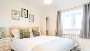Une chambre à coucher bien rangée, avec un lit, une table de chevet, une commode et une fenêtre avec des rideaux.