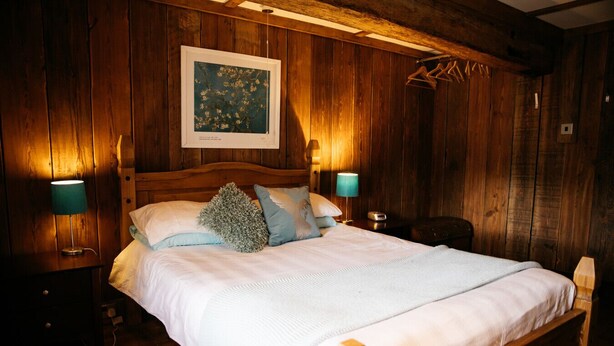 Een slaapkamer met houten lambrisering, een bed, twee bedlampjes en een ingelijst schilderij aan de muur.