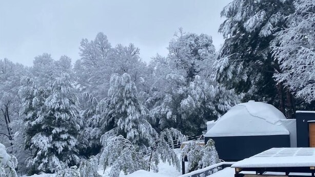 A snow-covered outdoor area with a wooden deck and a building with a large overhang. - HuellaBlanca Domos (Curacautin)
