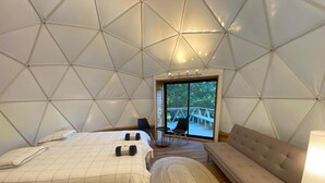 A modern, geometric-themed room with a bed, sofa, and a view of an outdoor deck. - HuellaBlanca Domos (Curacautin)