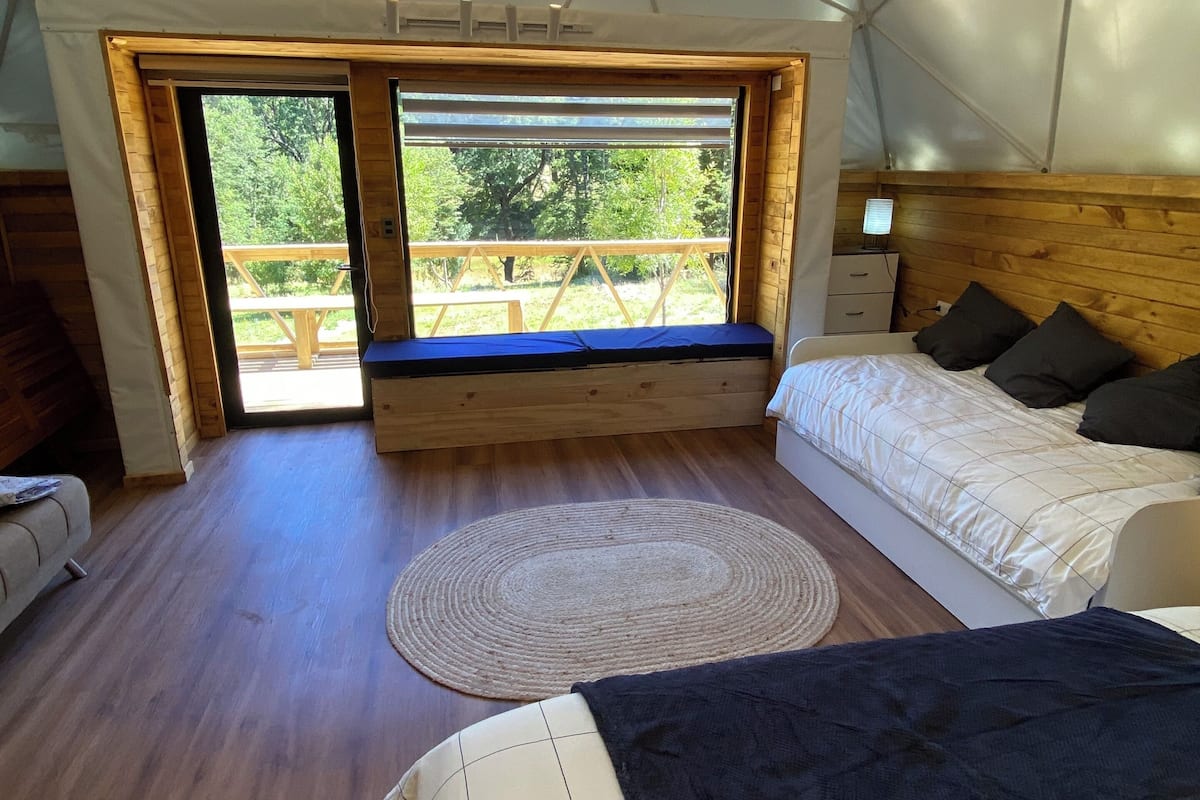A tented room with a bed, a bench, and a view of the outdoors.