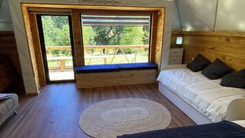 A tented room with a bed, a bench, and a view of the outdoors.