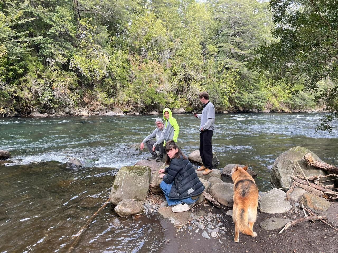 A group of people by a river with rocks and trees in the background.