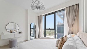 Un dormitorio moderno con una cama grande, un espejo redondo, una lámpara colgante y vistas de la ciudad a través de amplios ventanales.