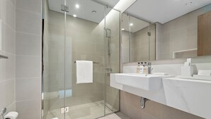 Un baño moderno con ducha envuelta en vidrio, un lavamanos blanco y encimera de mármol.