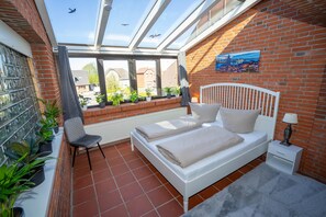 Un dormitorio con tragaluces, una cama, una silla y plantas en macetas.