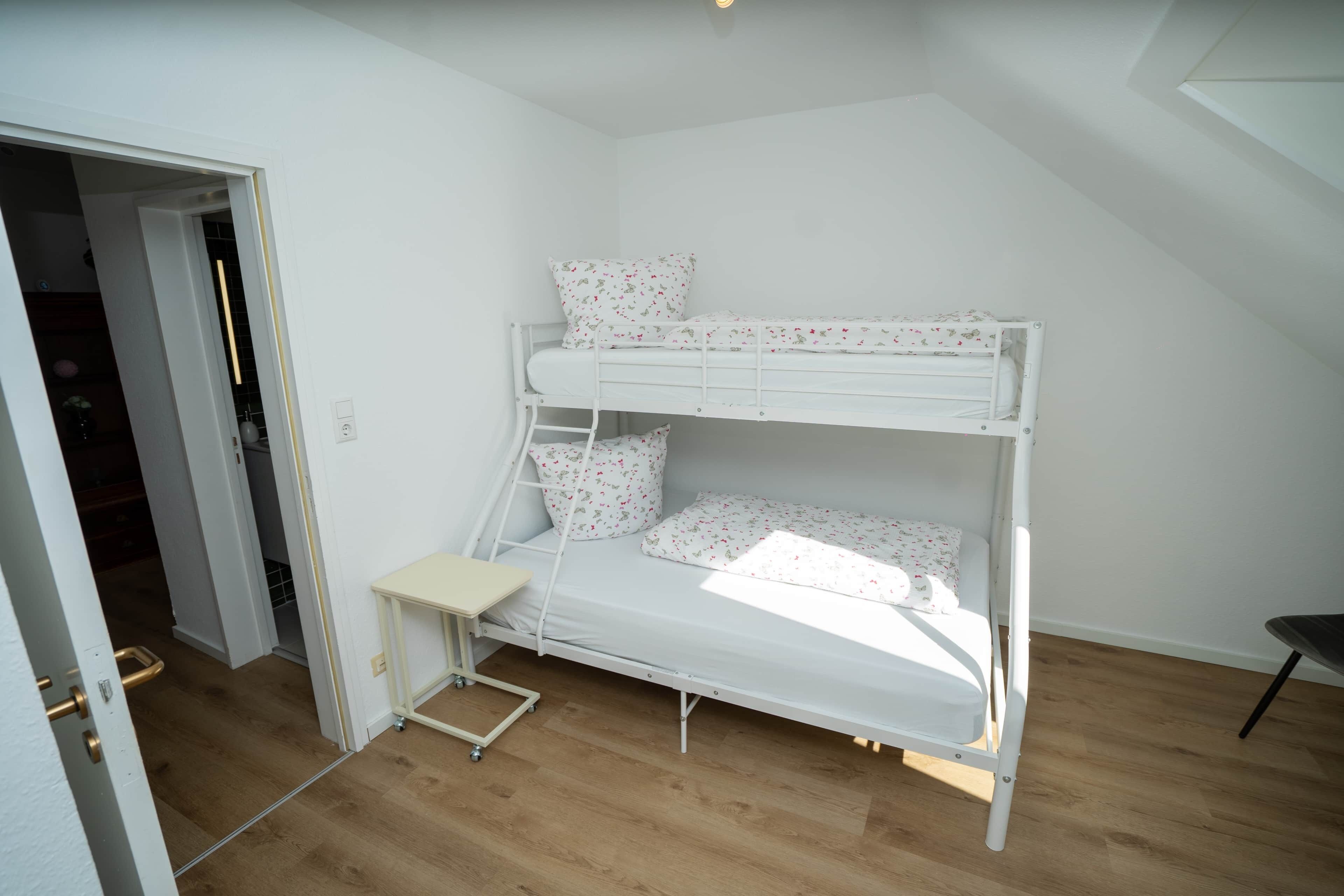 A bunk bed with a small desk in a room with wooden flooring and white walls.