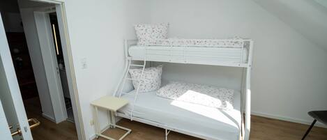A bunk bed with a small desk in a room with wooden flooring and white walls.