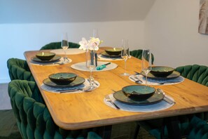 Una mesa de comedor con fuentes, platos y copas de vino, rodeada de sillas tapizadas de verde.