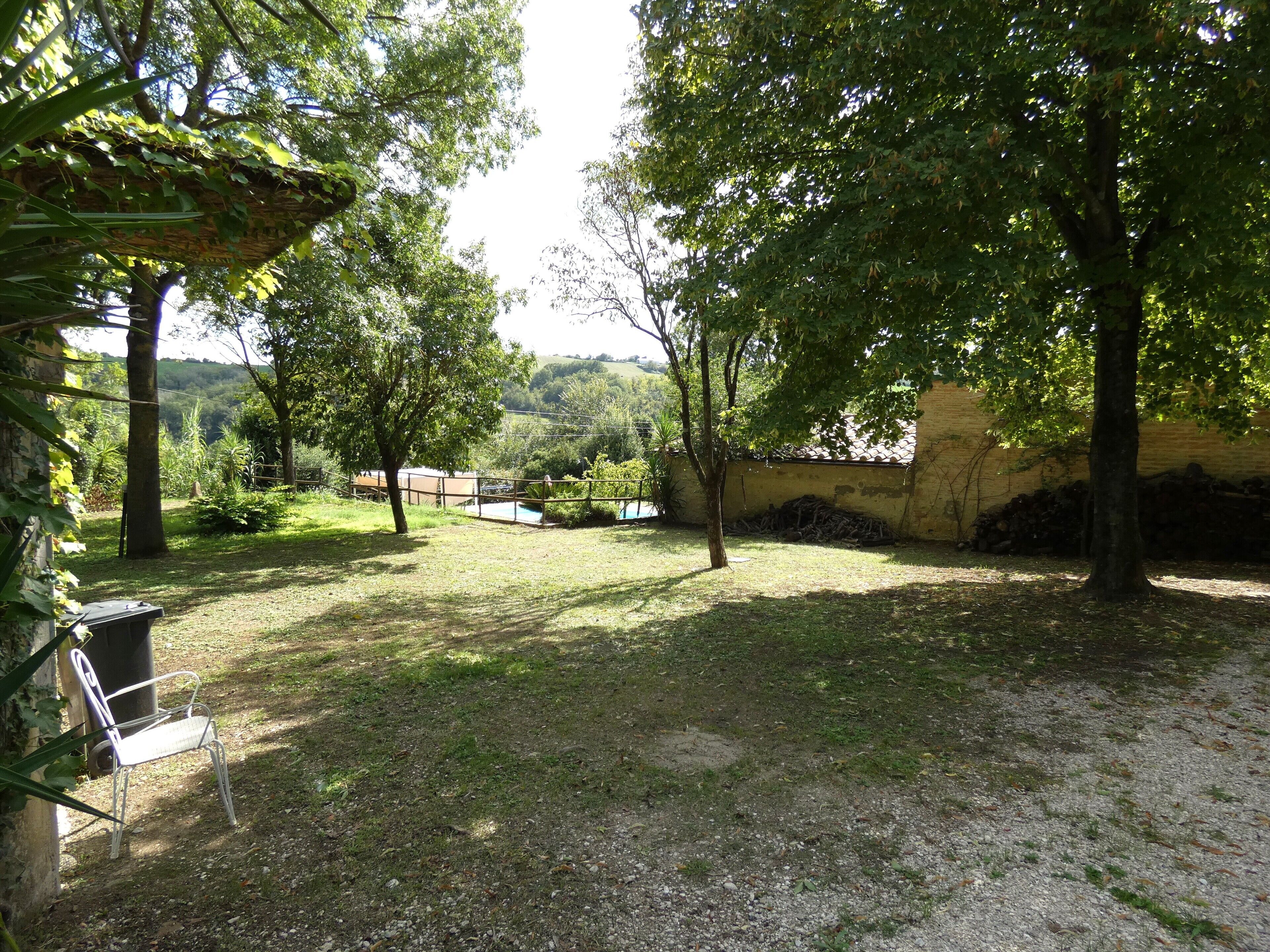 Un espace extérieur verdoyant, avec des arbres, une chaise en métal et un mur de pierre.