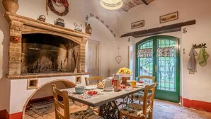 A rustic kitchen with a brick fireplace, a dining table set with chairs, and a green door with patterned curtains. - Scappo in Umbria, Il Maraldo (Narni)