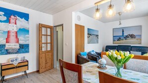 Un coin repas comprenant une table, des chaises, un vase de tulipes, une radio et un tableau représentant un phare.