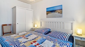 Une chambre à coucher comprenant un lit, une table de chevet, une chaise, une armoire et un tableau accroché au mur.