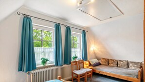 A room with a bed, a sofa, a chair, a window with curtains, a radiator, and a plant. - Apartment 2, Upper Floor with Wi-Fi (Hooksiel)