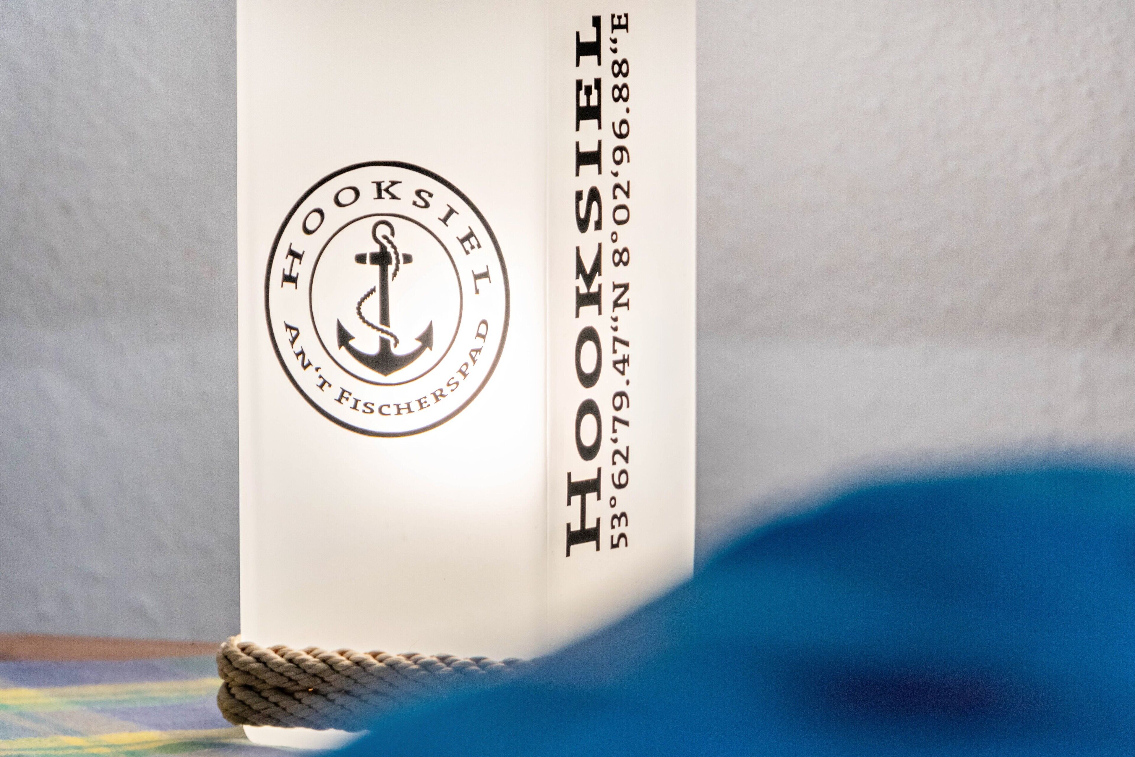A vertical object with a logo and text, including 'HOOKSIEL AN FISCHERSTAPAD' and a phone number.
