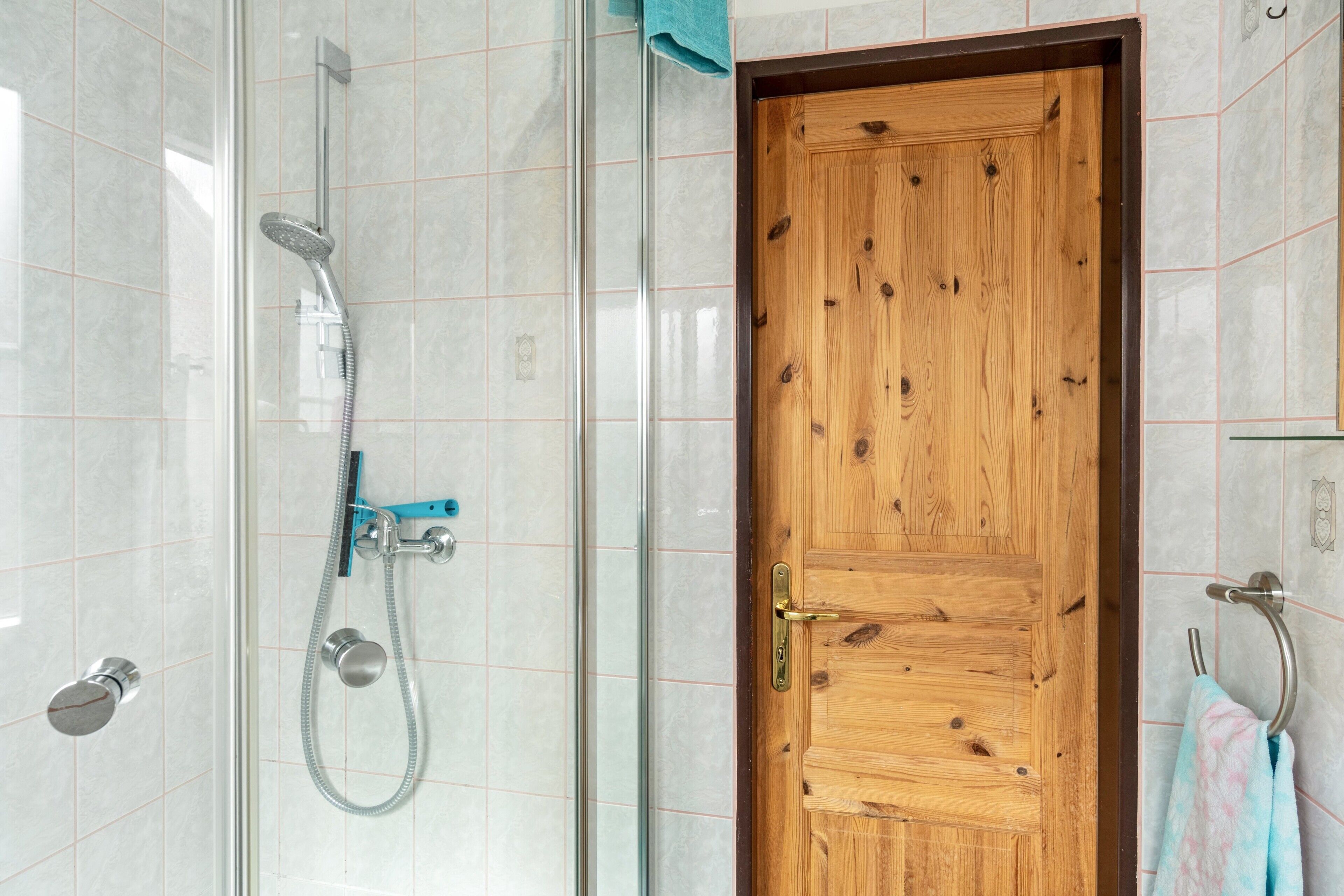 A bathroom with a glass shower enclosure, a wooden door, and a towel rack.