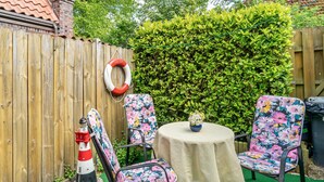 A wooden fence, a lifebuoy, a lighthouse model, and two floral chairs with a round table in a garden setting. - Apartment 2, Upper Floor with Wi-Fi (Hooksiel)