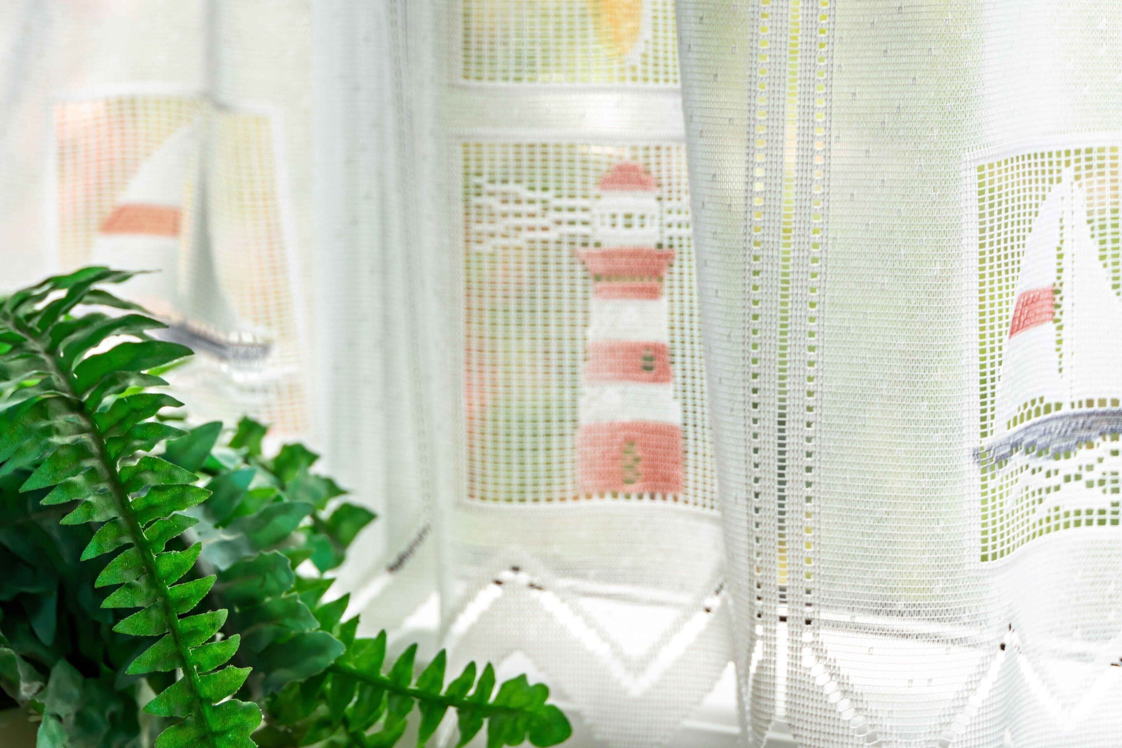 A window with a white lace curtain featuring a lighthouse design.