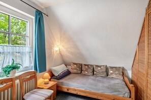 Una habitación acogedora con una cama de madera, una mesita con una lámpara, una silla y una ventana con cortinas.