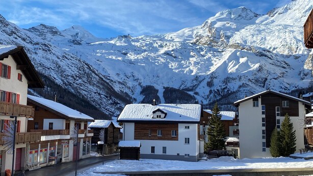 Un pueblo montañoso cubierto de nieve con casas de madera tradicionales y un edificio moderno.