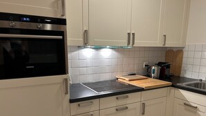 Una cocina con armarios blancos, un horno negro y una tabla de cortar de madera sobre la encimera.