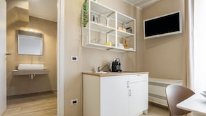 Ein modernes Badezimmer mit Waschbecken, Spiegel und Regalen über der Ablage. Ein Flachbildfernseher ist an der Wand montiert und ein Sessel steht in der Nähe eines Tisches.
