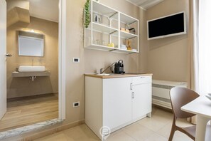 Ein modernes Badezimmer mit Waschbecken, Spiegel und Regalen über der Ablage. Ein Flachbildfernseher ist an der Wand montiert und ein Sessel steht in der Nähe eines Tisches.