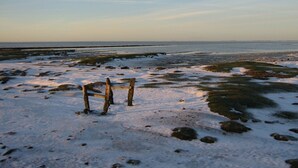 Eine hölzerne Bank an einem verschneiten Strand mit Blick auf den Ozean.